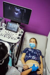 Woman with face mask at ultrasound examination during COVID-19
